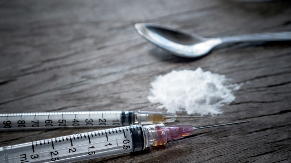 A spoon and two syringes next to a pile of heroin on a table