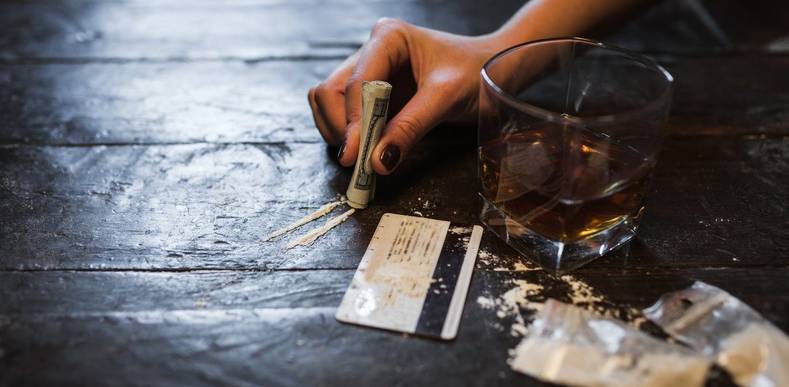 person preparing a line of cocaine next to glass of alcohol