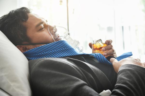Person lying down with oxygen mask and drinking.