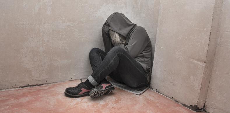 Person wearing a hoodie siting on the ground covering their face with their hands.