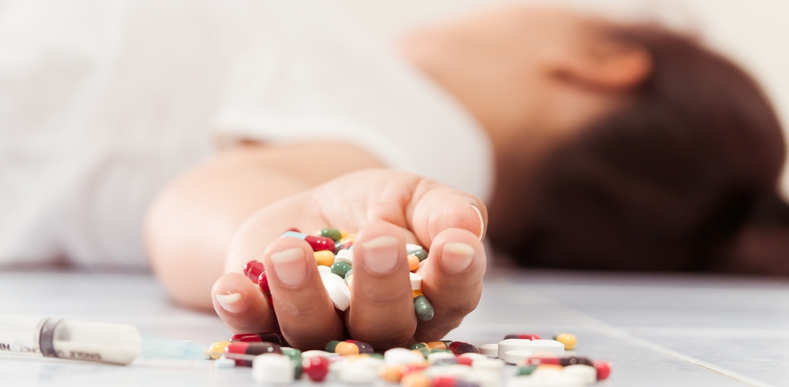 Person lying on the ground with pills in the palm of their hand.