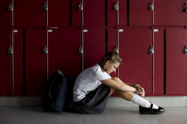 Teenage girl sitting on the floor next to a set of lockers.