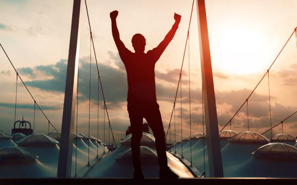 Person on the bow of a boat with their hands raised.