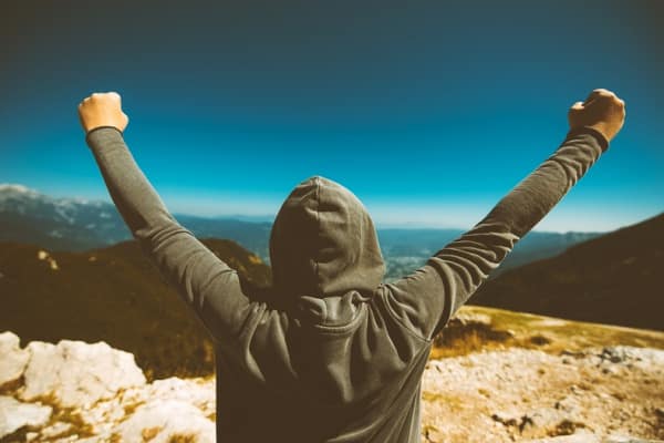 hiker at top of mountain raising arms with joy