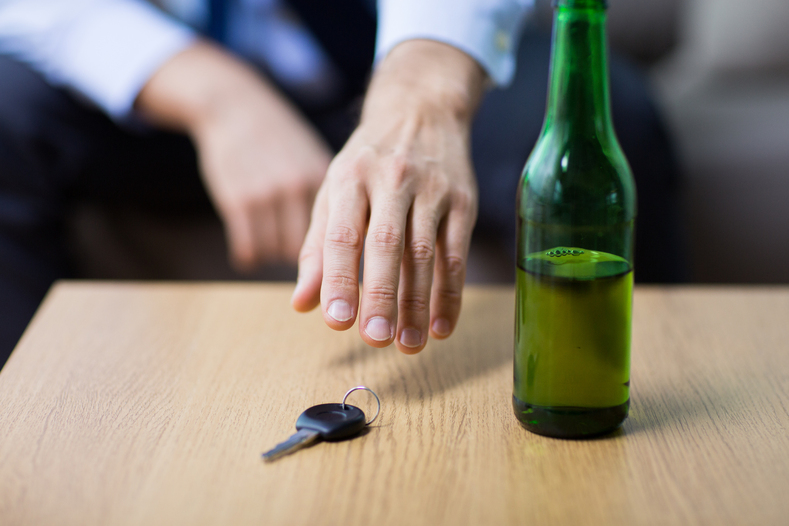 A man's hand reaches for car keys next to a bottle of alcohol, despite the fact that drinking and driving is a dangerous and deadly symptom of alcohol misuse. 