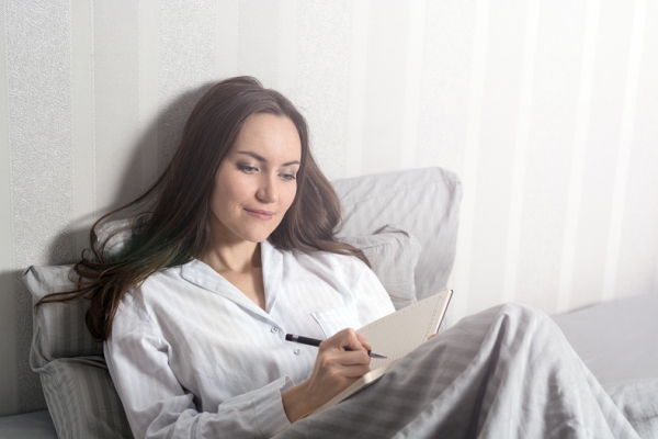A woman sitting in bed while writing in a journal