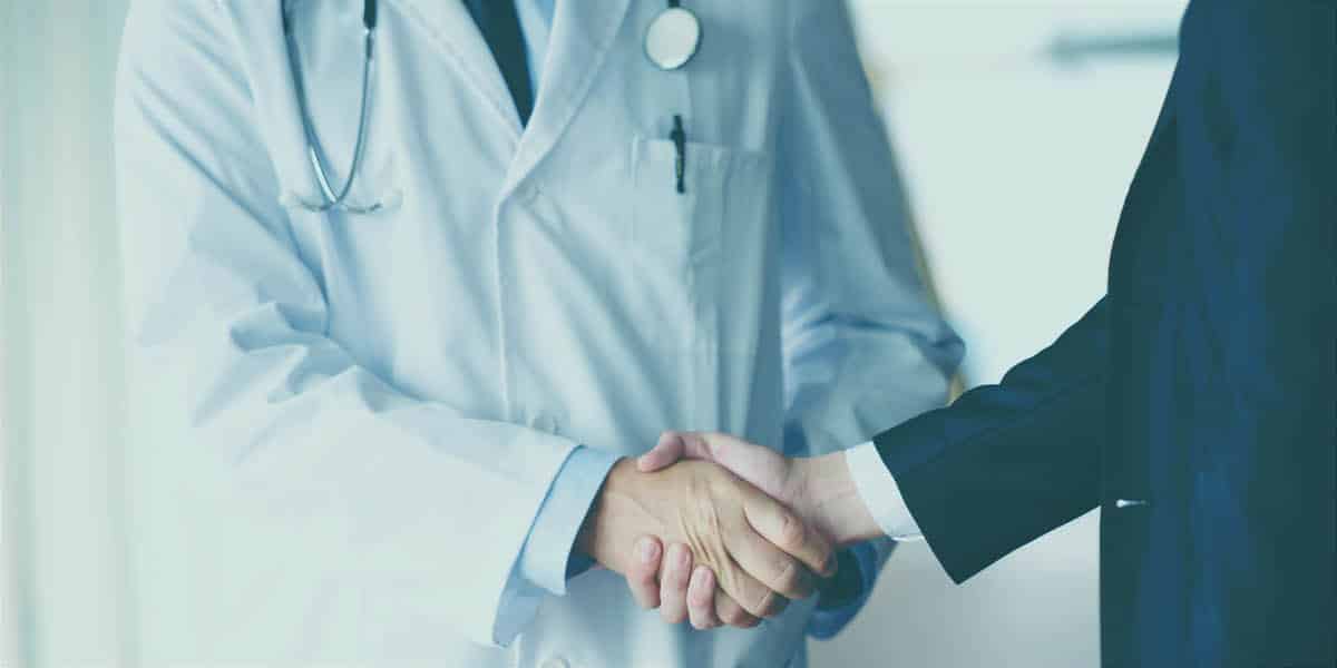 A doctor and an insurance representative shake hands and discuss rehab treatment