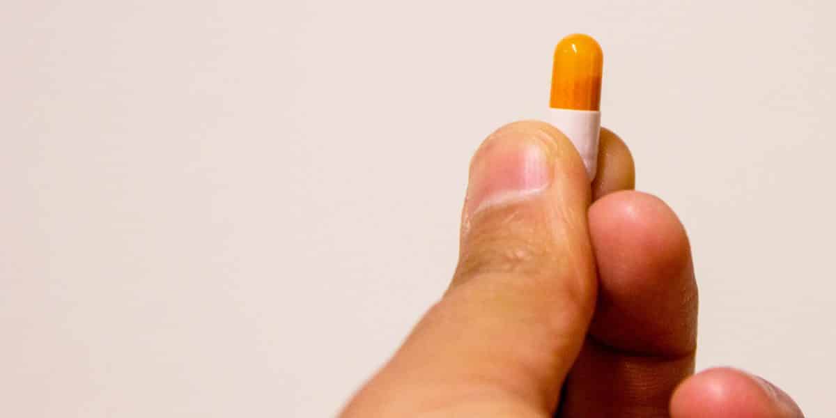 Person holding an orange and white adderall pill