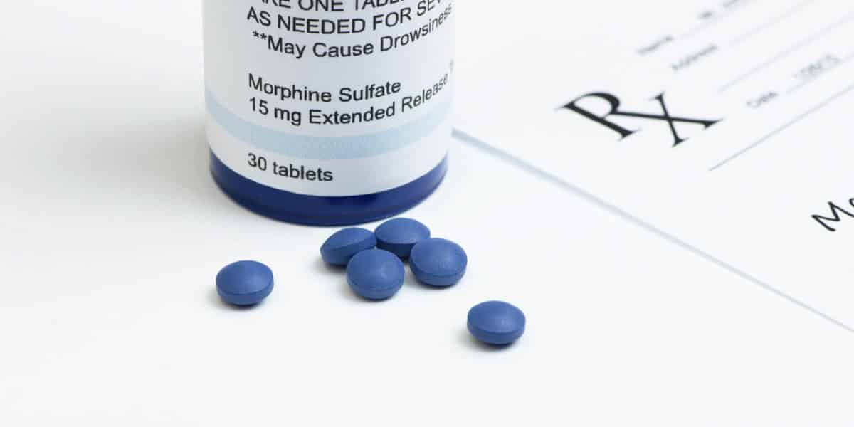 Morphine pills next to a prescription bottle and a doctors paper prescription