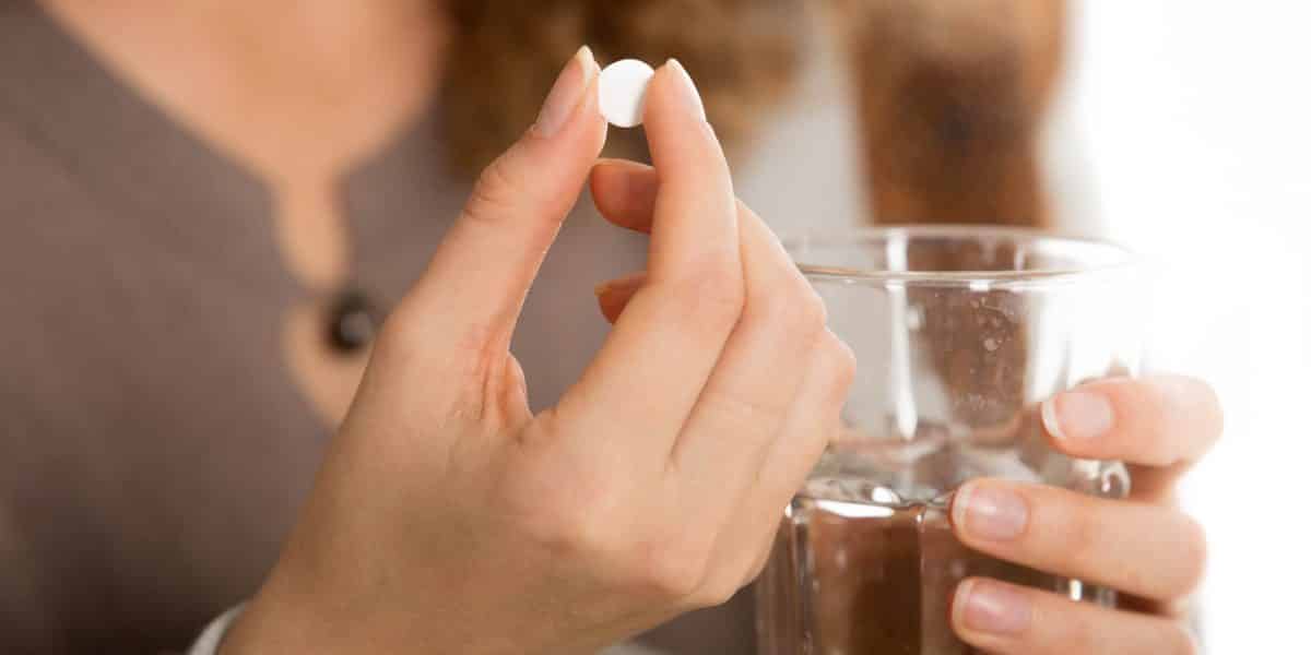 woman holding oxycodone pill in one hand and glass of water in the other