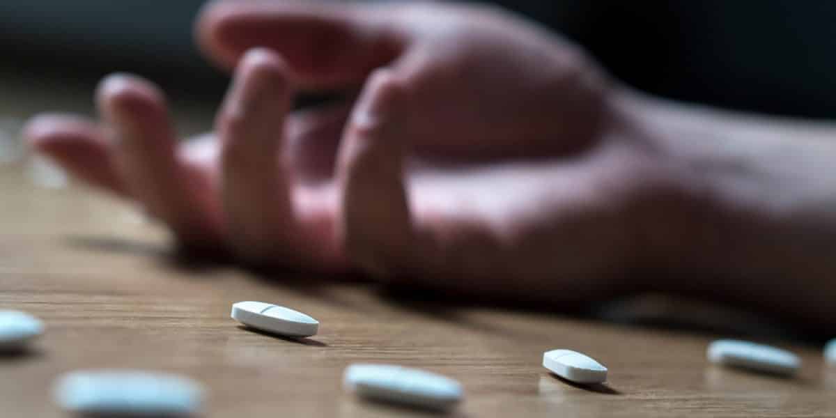 Person laying on the ground next to scattered hydrocodone pills after overdosing