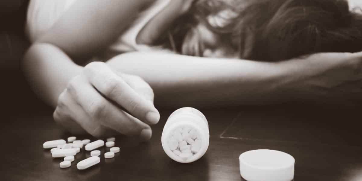 Person passed out on the ground near a pile of morphine pills and prescription bottle after overdosing