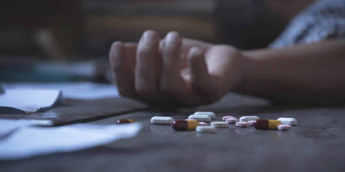 Person laying on the ground near scatterd opioid pills after overdosing
