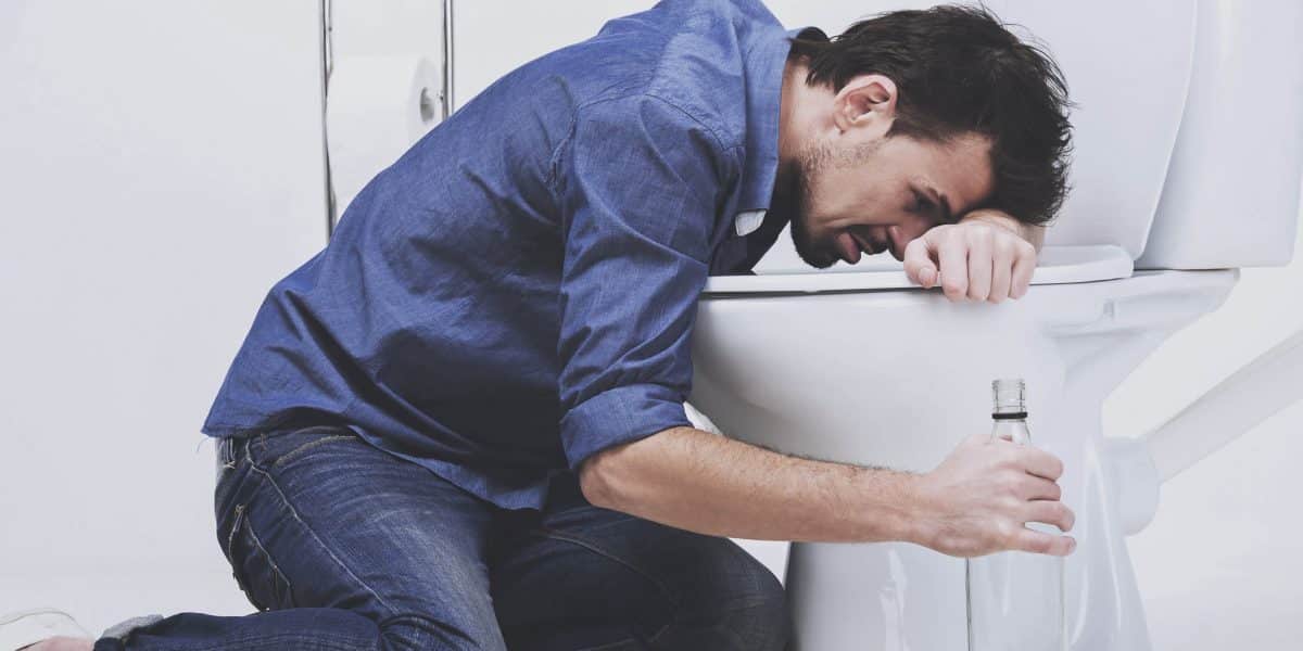 man experiencing alcohol poisoning hunched over toilet holding empty bottle