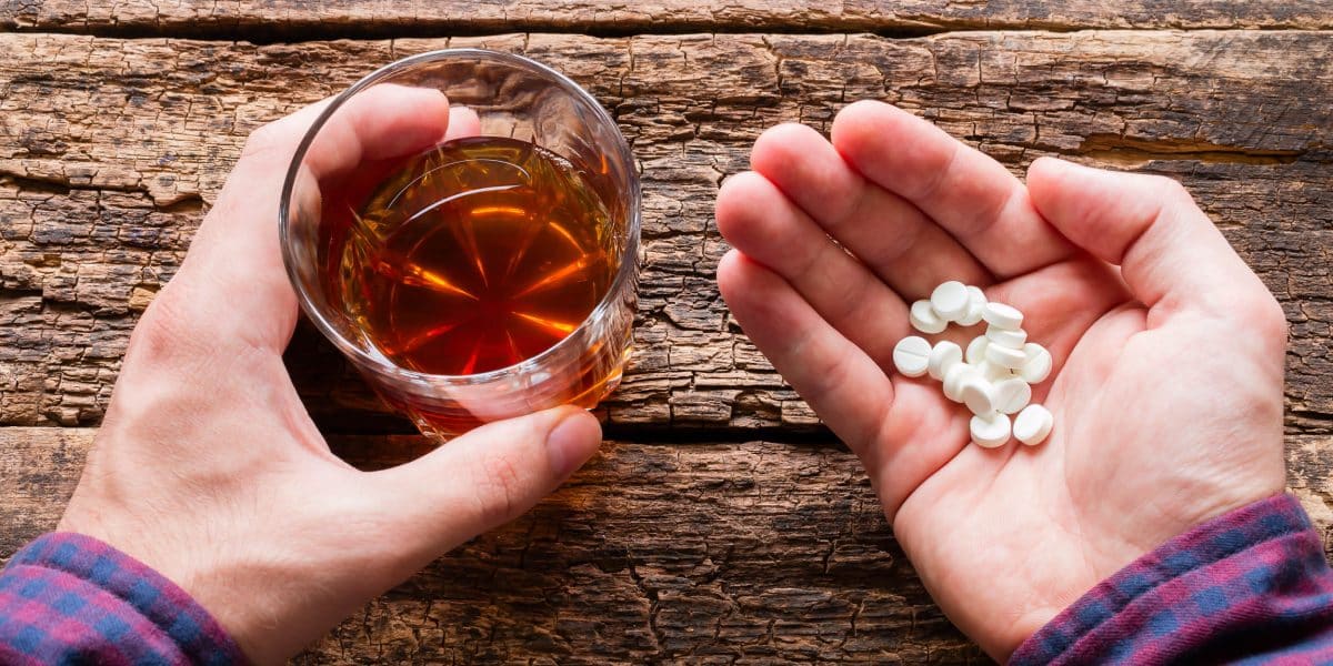 Person holding oxycontin pills in one hand and a glass of alcohol in the other