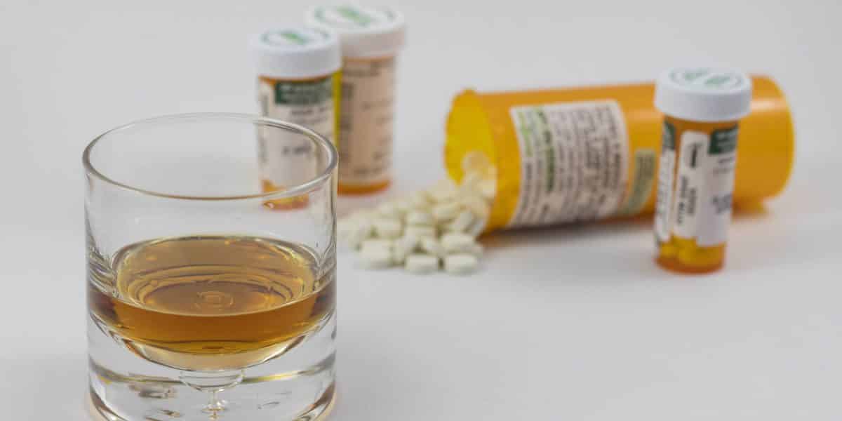 Vicodin pills in multiple prescription bottles with some spilled on a counter next to a glass of alcohol