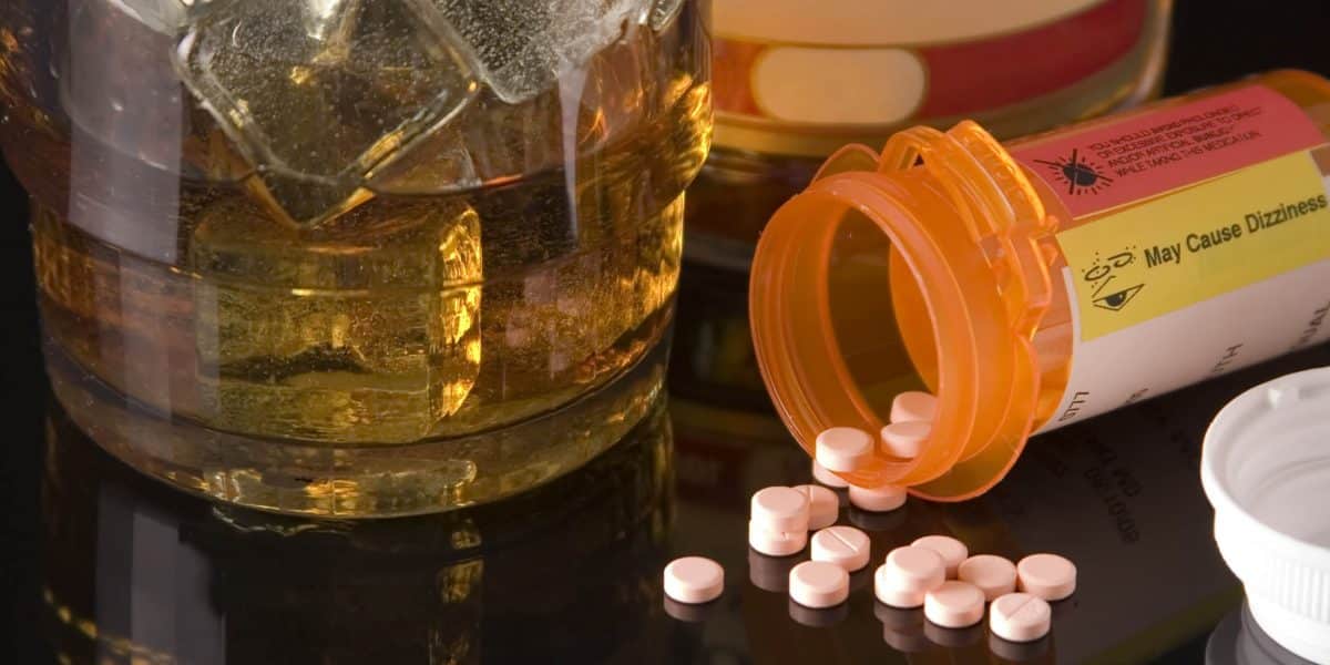Xanax pills spilling out of an orange prescription bottle next to a glass of alcohol