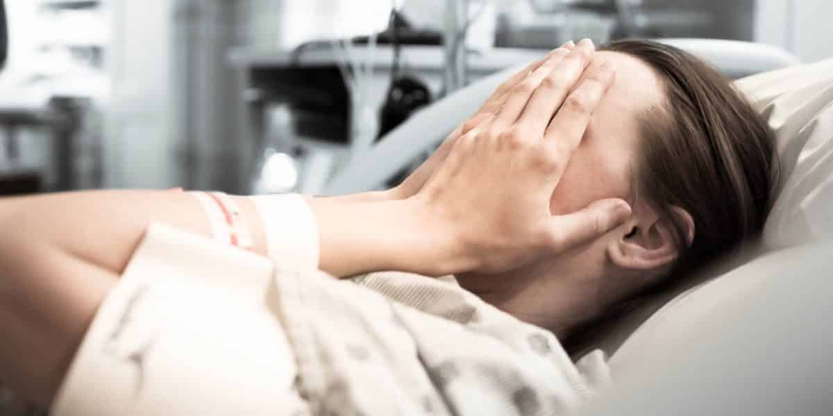 Woman laying down in a hospital bed with her hands covering her face while experiencing vicodin withdrawal
