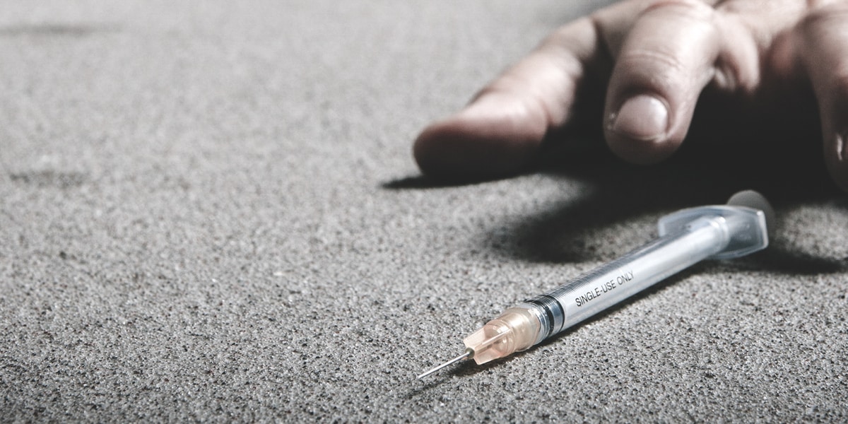 person reaching for heroin needle