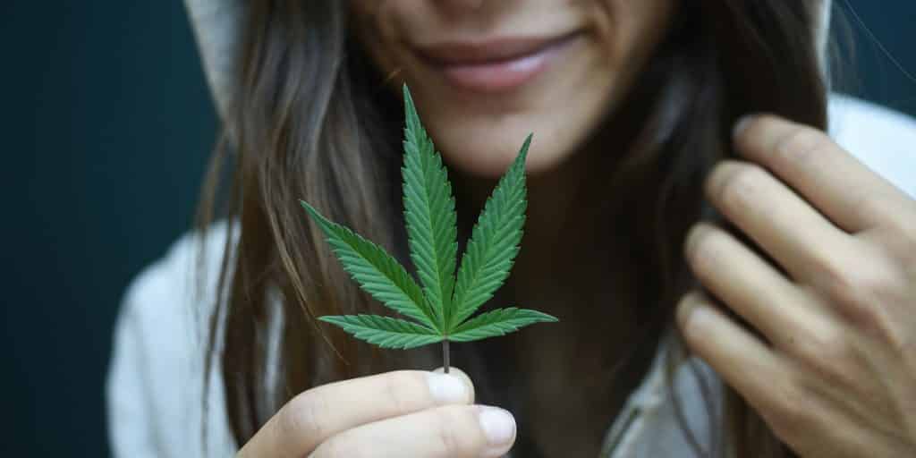 Woman in hood holding marijuana leaf