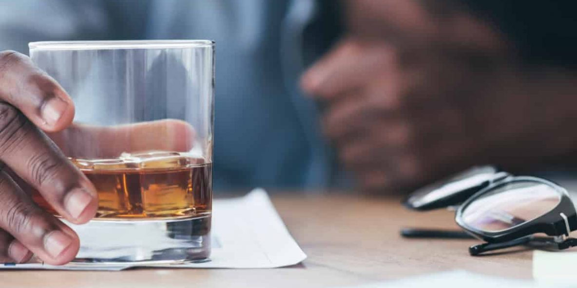 employee, hand grasping glass of alcohol with head down on work desk