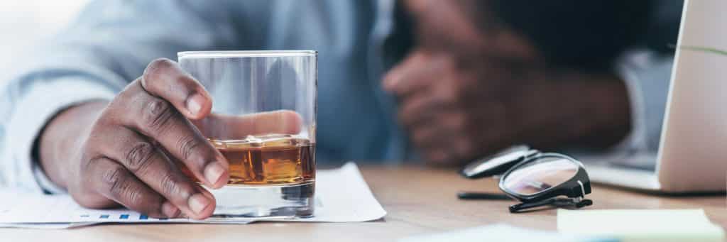 employee, hand grasping glass of alcohol with head down on work desk